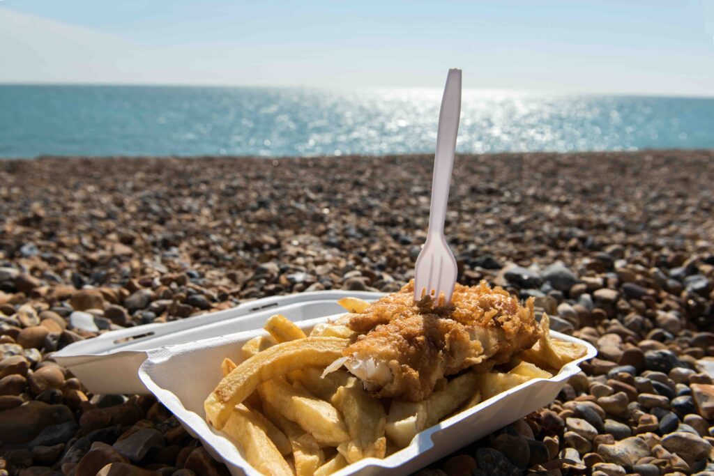 fish and chips in a box on a shingle beach