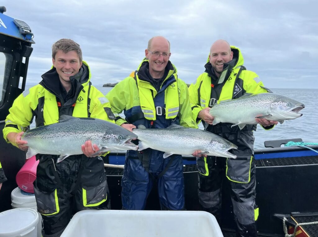 Three men in life jackets, each holding a salmon