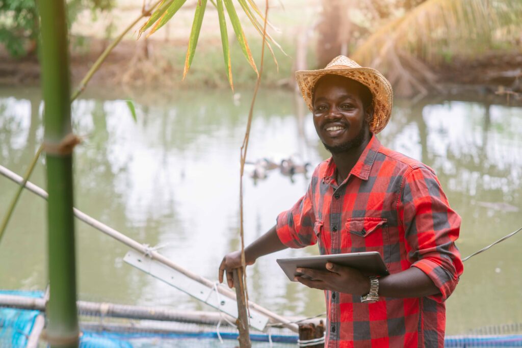 Man with hat holding tablet by side of fish farm pond